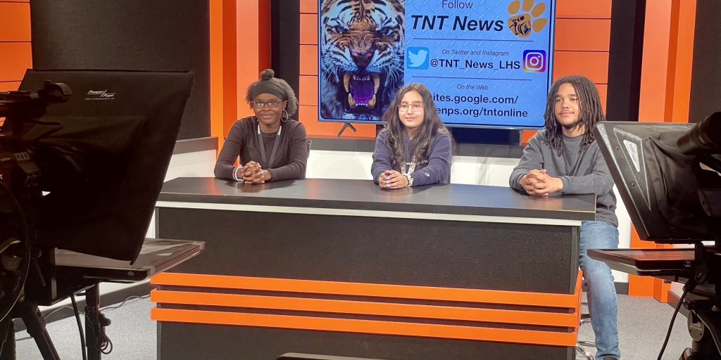 three students at TV news desk