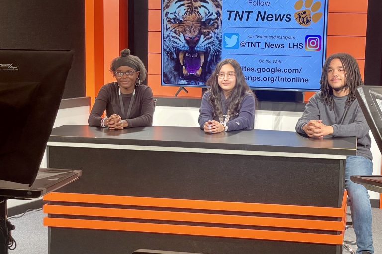 three students at TV news desk